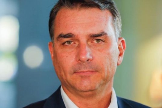 Flávio Bolsonaro em close, sério, sem olhar para a câmera