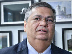 ministro Flávio Dino com expressão pensativa, sem olhar para a câmera, de óculos de grau, em close