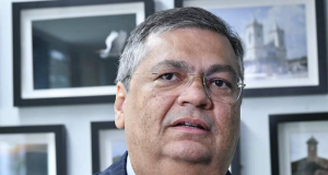 ministro Flávio Dino com expressão pensativa, sem olhar para a câmera, de óculos de grau, em close