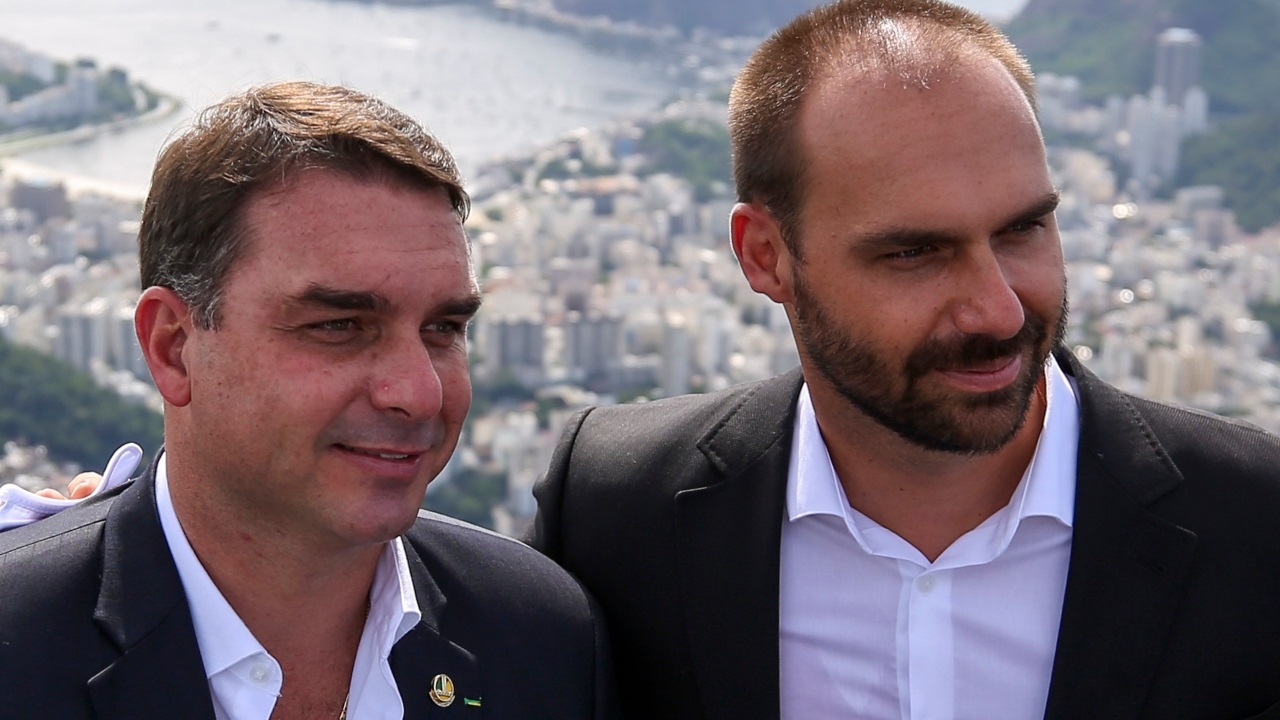 O senador Flávio Bolsonaro (PL-RJ) e o ex-deputado federal Eduardo Bolsonaro (PL-SP) em close, lado a lado, sem olhar para a câmera