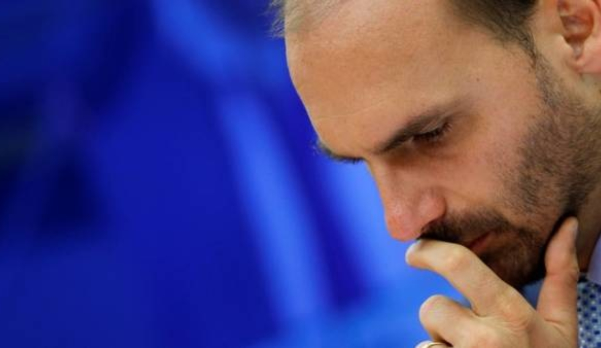 O ex-deputado Eduardo Bolsonaro no canto direito de foto, cabisbaixo, sério