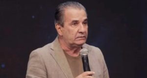 pastor Silas Malafaia de roupa social bege, olhando para o lado, sério, segurando microfone