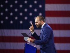 ex-deputado Eduardo Bolsonaro (PL-SP) em pé, falando e apontando, com bandeira dos EUA ao fundo