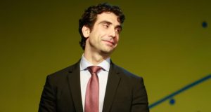 Gabriel Galípolo de terno e gravata, olhando para o lado com sorriso tímido