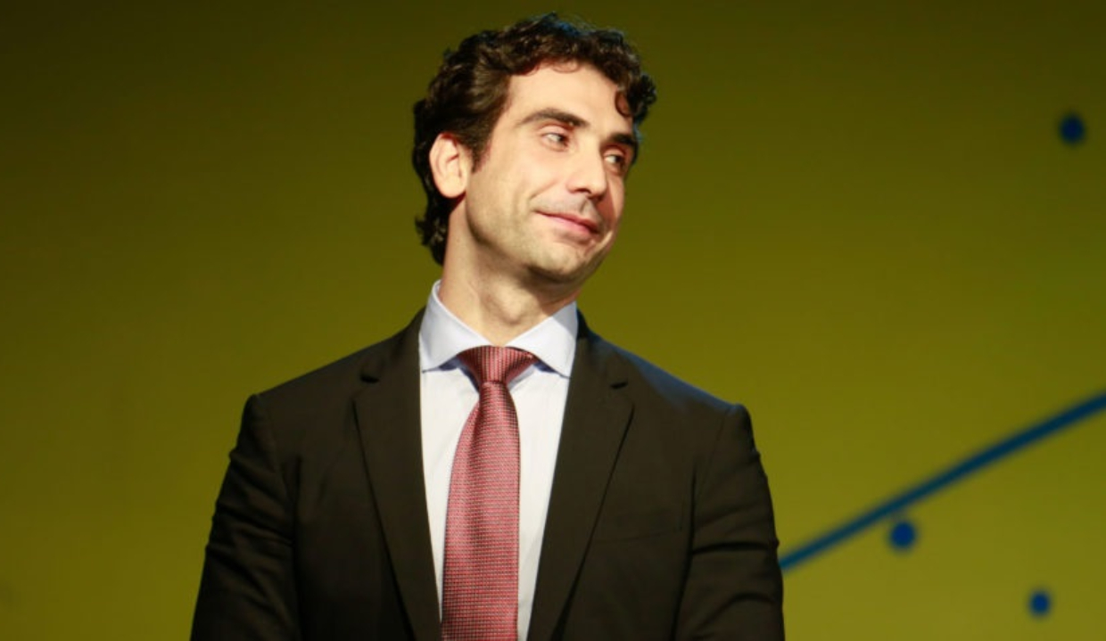 Gabriel Galípolo de terno e gravata, olhando para o lado com sorriso tímido