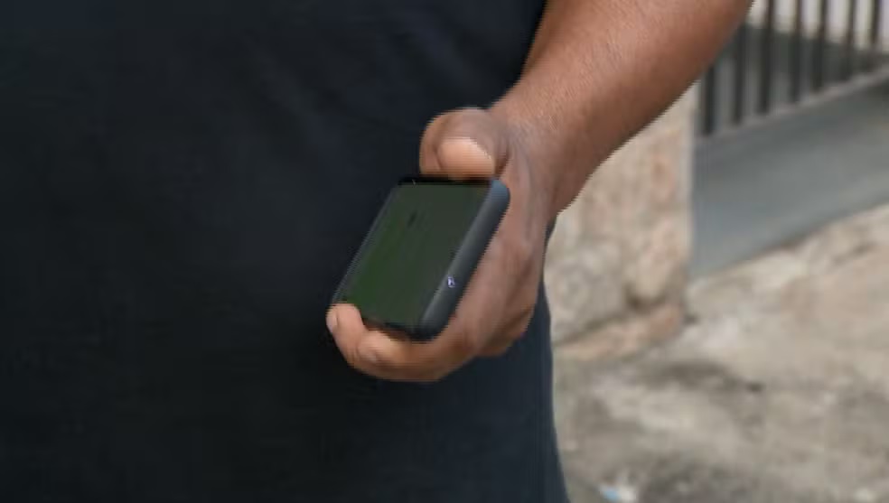 Homem de camiseta preta segurando celular, sem aparecer o rosto