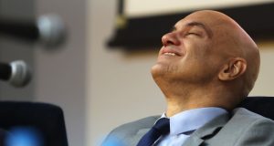 Alexandre de Moraes sorrindo, de olhos fechados, no canto esquerdo de foto