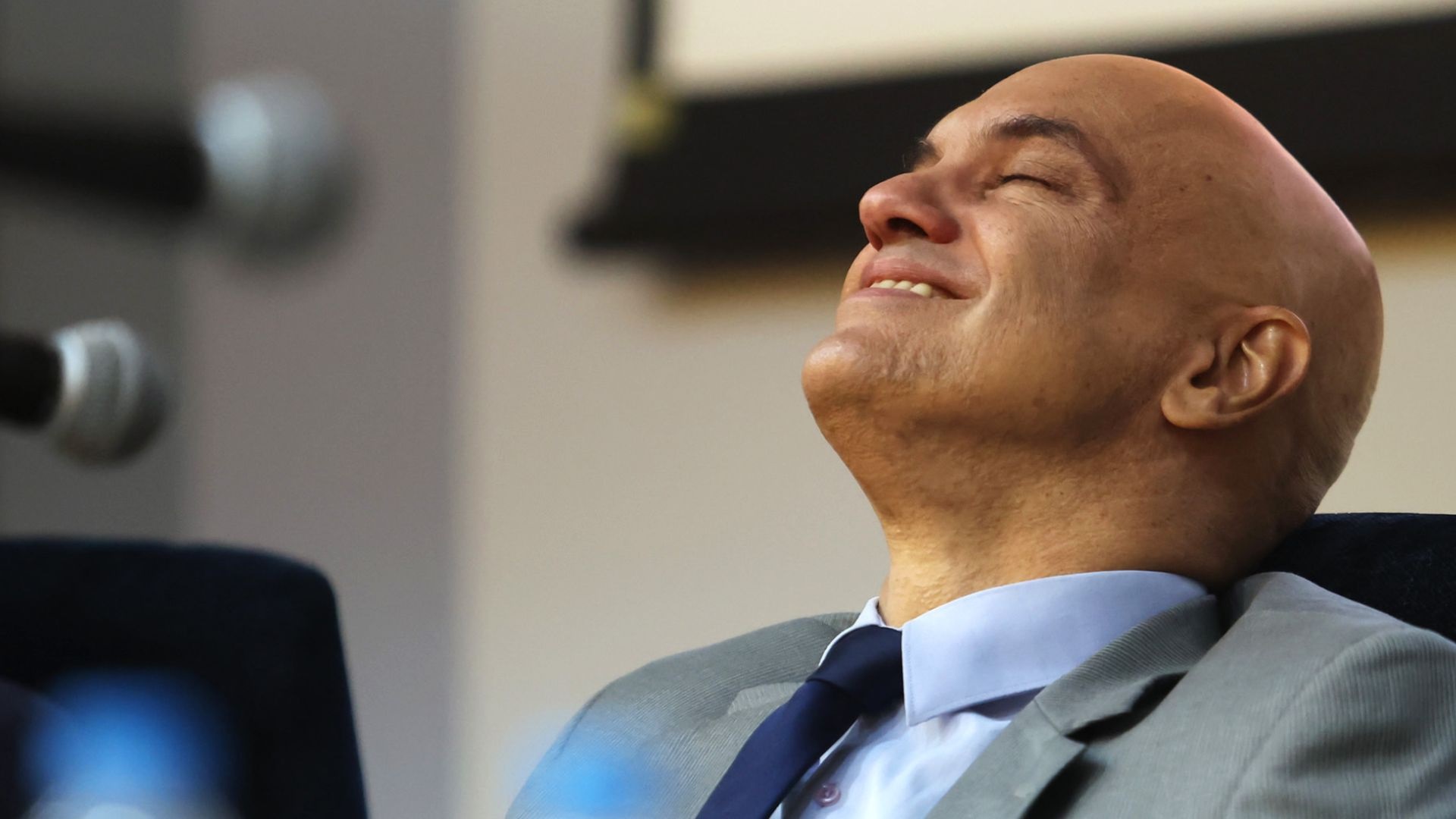 Alexandre de Moraes sorrindo, de olhos fechados, no canto esquerdo de foto