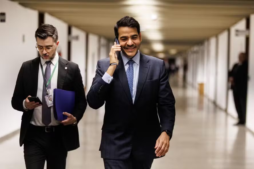 Jorge Messias circulando pelo Senado, andando, sorrindo e falando ao telefone