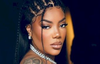 Ludmilla em close, olhando para a câmera, séria