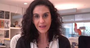 Malu Gaspar de cabelo solto, com roupa preta e branca, falando para a câmera