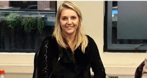 Mariângela Fialek de cabelo solto e roupa de frio preta, sentada, sorrindo para a câmera