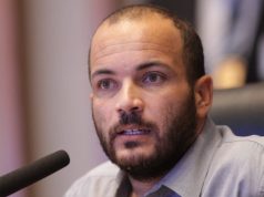 Alan Diego dos Santos Rodrigues sério, falando em microfone, em close