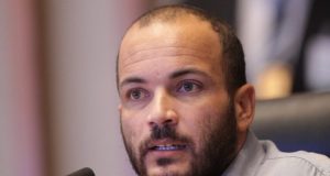 Alan Diego dos Santos Rodrigues sério, falando em microfone, em close