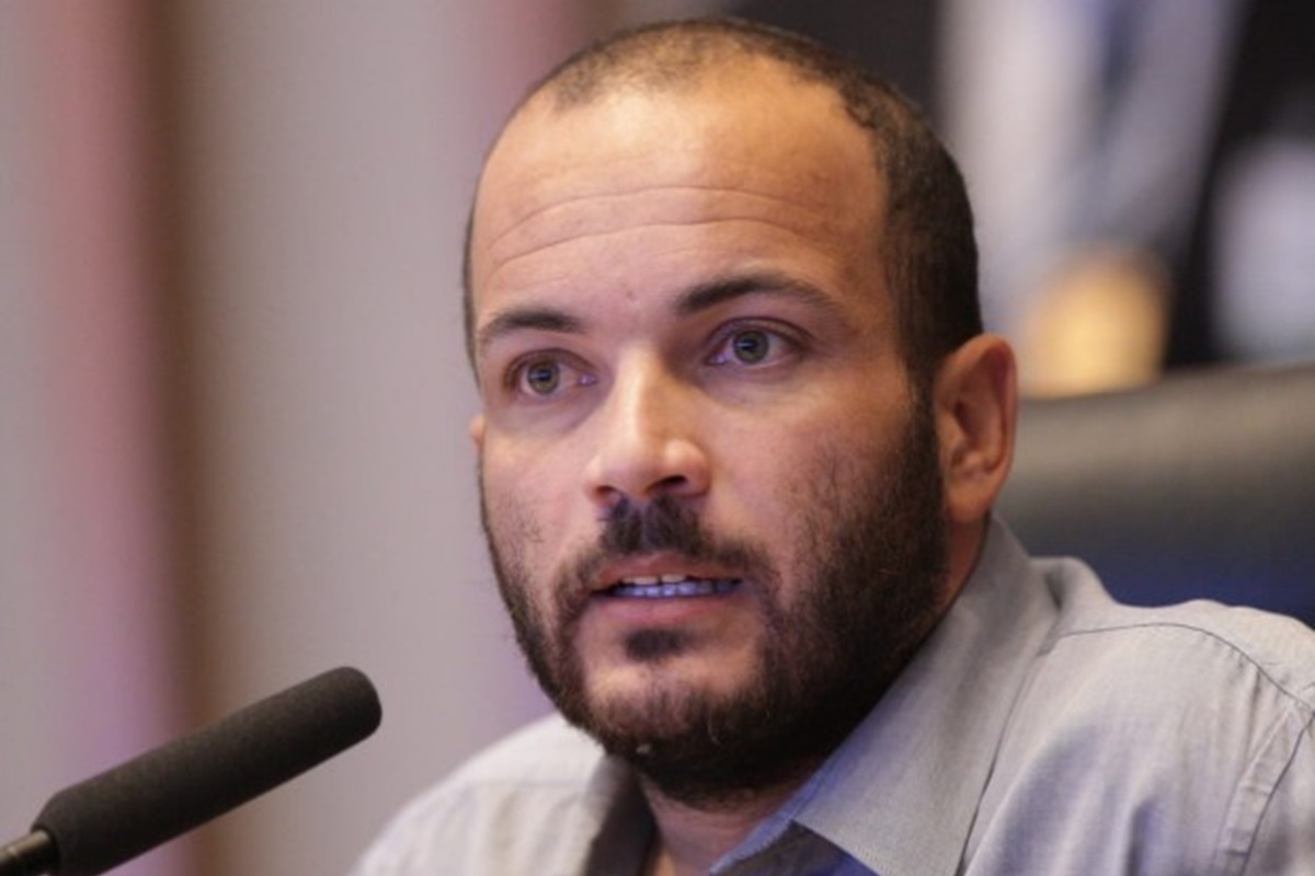 Alan Diego dos Santos Rodrigues sério, falando em microfone, em close