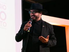 Dudu Morais, advogado, poeta e influenciador digital, falando e gesticulando em microfone, de roupa e chapéu pretos, olhando para o lado, sério