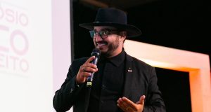 Dudu Morais, advogado, poeta e influenciador digital, falando e gesticulando em microfone, de roupa e chapéu pretos, olhando para o lado, sério