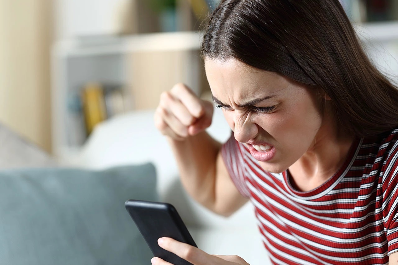 Mulher de cabelo solto e camiseta listrada, gritando com cara de raiva pro celular
