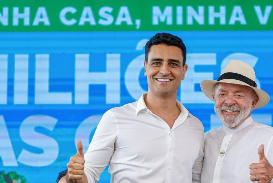 O prefeito de Maceió, João Henrique Caldas, e o presidente Luiz Inácio Lula da Silva (PT), de camisas sociais brancas, sorrindo lado a lado e fazendo joinha para a câmera; Lula de chapéu