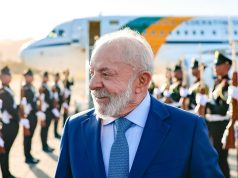 O presidente Luiz Inácio Lula da Silva (PT) sorrindo e olhando para o lado, com avião ao fundo