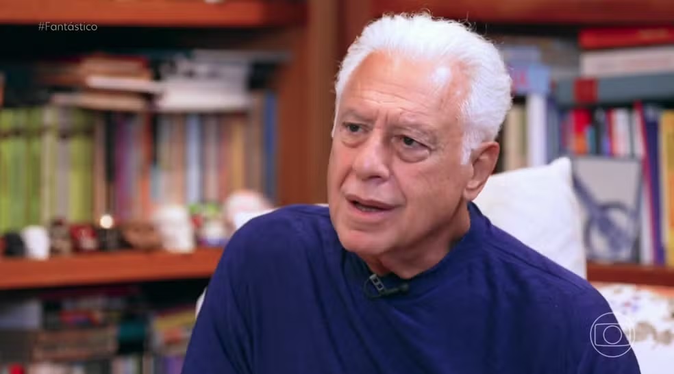 Antonio Fagundes de roupa de frio azul marinho, falando, sério, sem olhar para a câmera