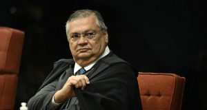 ministro Flávio Dino sério, olhando para o lado, de preto, sentado