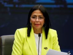 Delcy Rodríguez, presidente interina da Venezuela, de óculos de grau e roupa social branca e amarela, falando em microfone, de cabelo solto, sem olhar para a câmera
