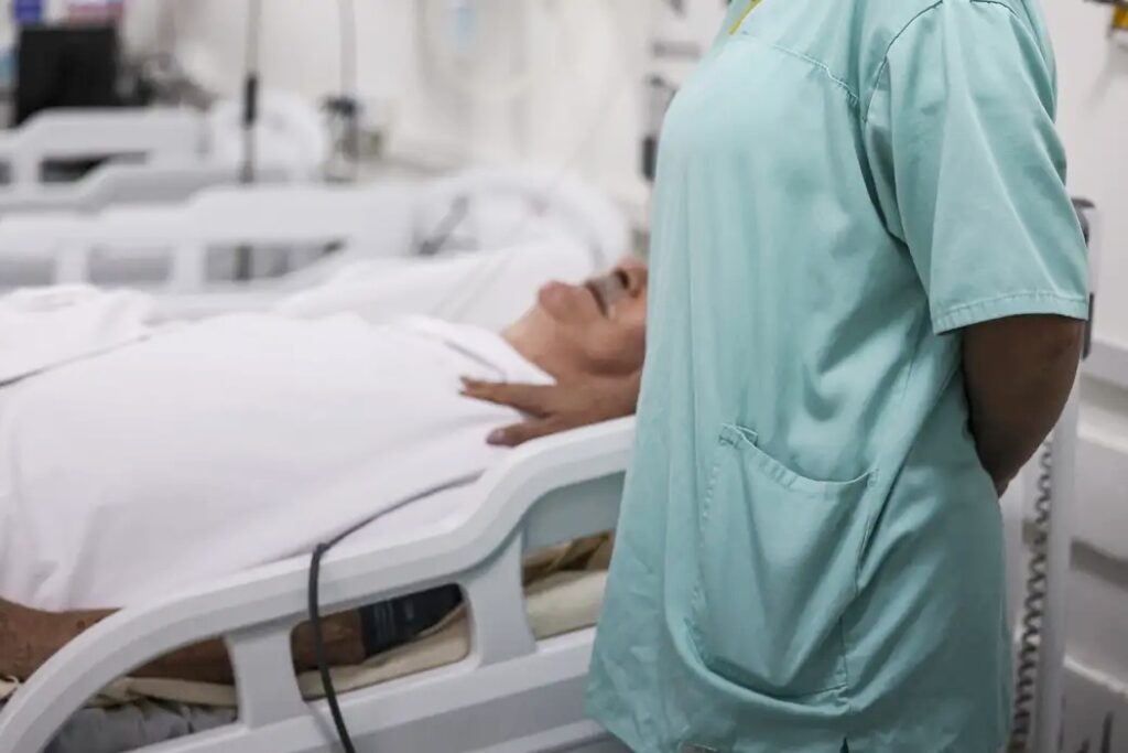 Pessoa de roupa hospitalar deitada ao lado de paciente