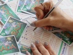 Mãos com unhas pintadas preenchendo talões da Mega da Virada