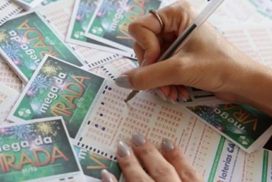 Mãos com unhas pintadas preenchendo talões da Mega da Virada