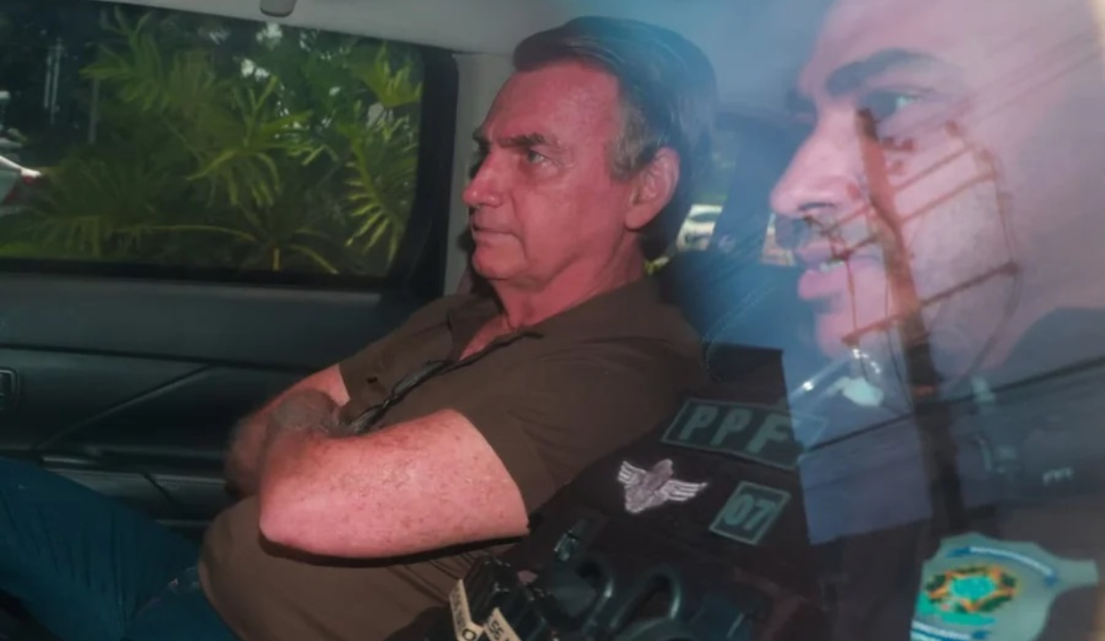 ex-presidente Jair Bolsonaro dentro de carro, sério, sentado, de braços cruzados, de camisa polo marrom