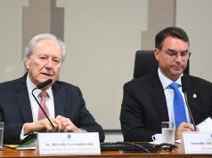 Ricardo Lewandowski e Flávio Bolsonaro sentados lado a lado, sérios