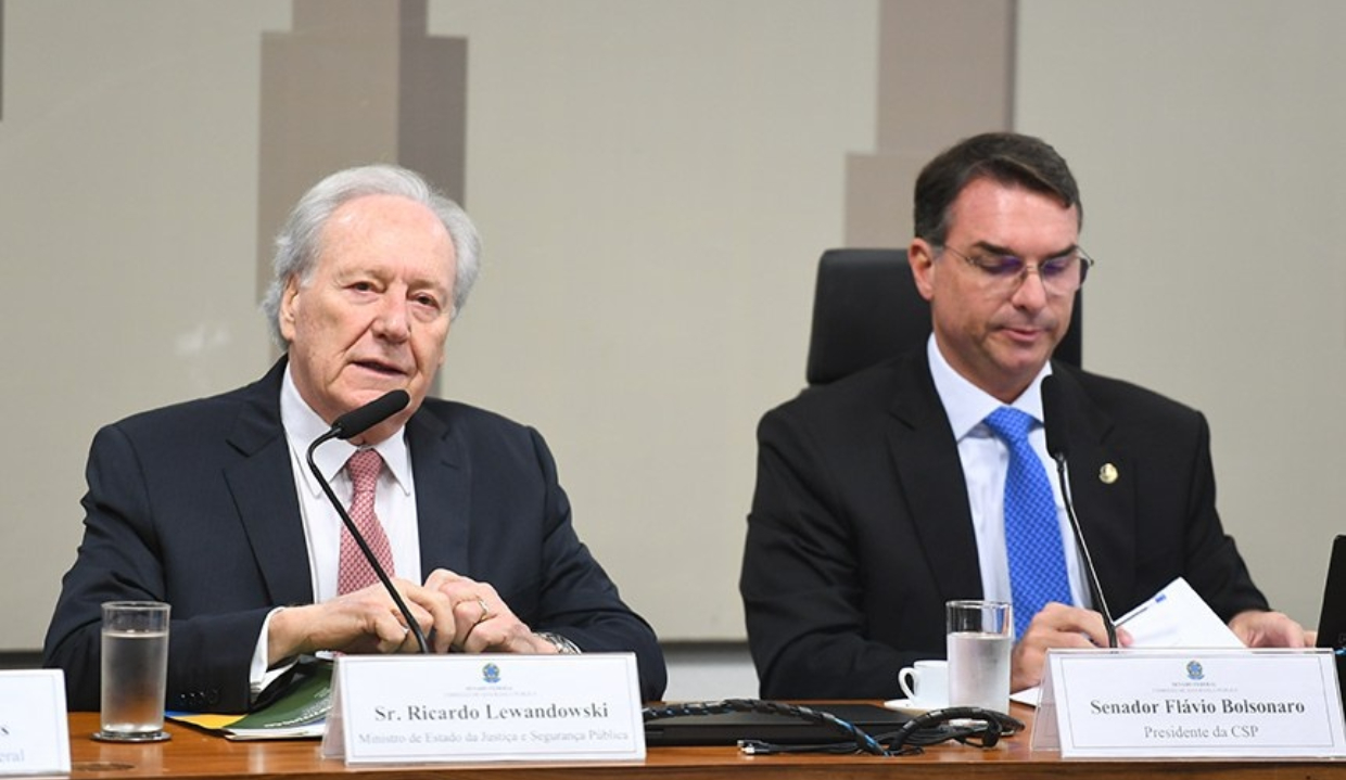 Ricardo Lewandowski e Flávio Bolsonaro sentados lado a lado, sérios