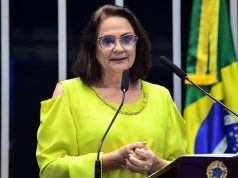 A senadora Damares Alves (Republicanos-DF) falando em microfone, de roupa amarela e óculos de grau