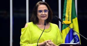A senadora Damares Alves (Republicanos-DF) falando em microfone, de roupa amarela e óculos de grau