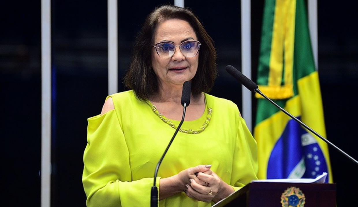 A senadora Damares Alves (Republicanos-DF) falando em microfone, de roupa amarela e óculos de grau