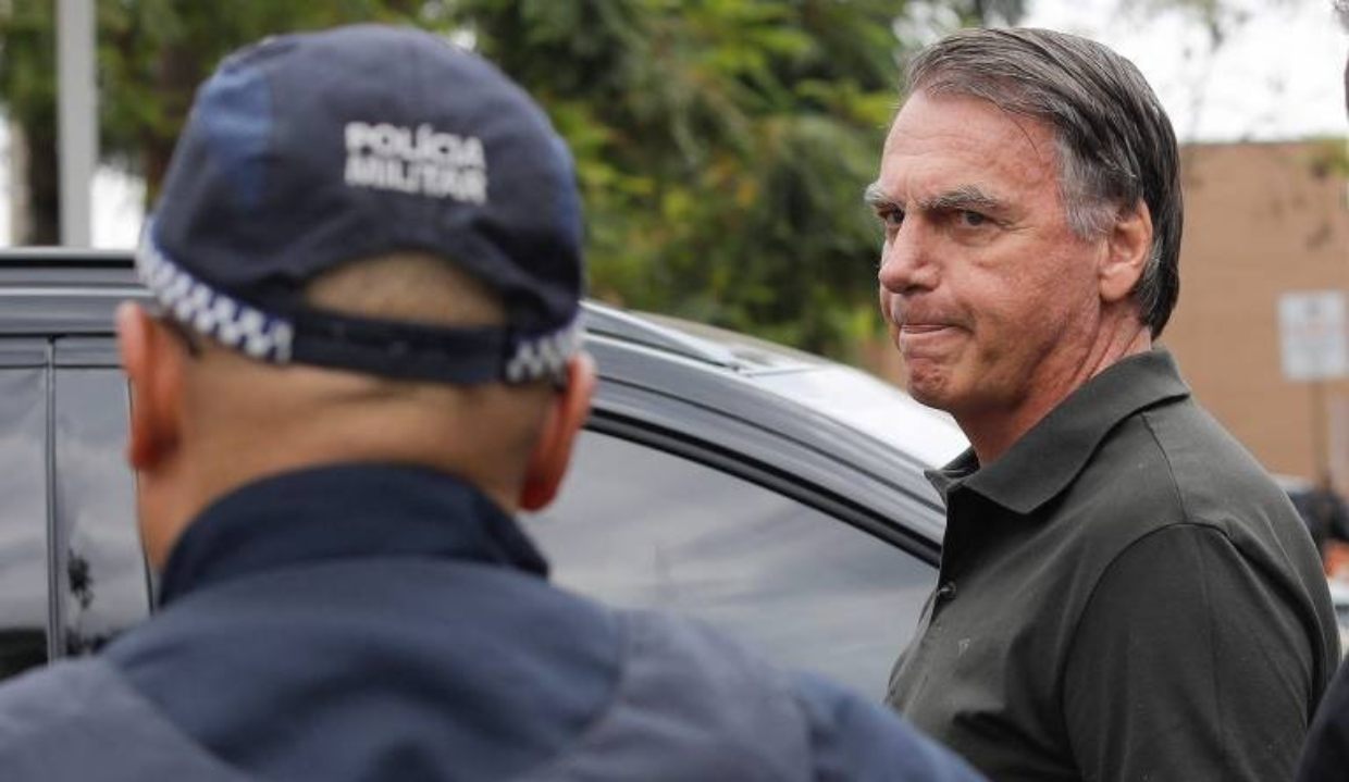O ex-presidente Jair Bolsonaro (PL) sério, perto de policial, que está de costas