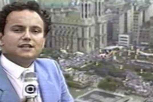 O jornalista Ernesto Paglia em registro da década de 80, no canto esquerdo de foto, falando em microfone da Globo