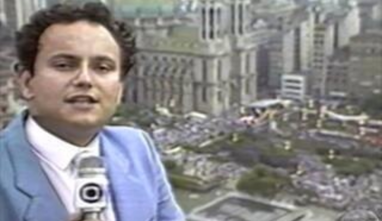 O jornalista Ernesto Paglia em registro da década de 80, no canto esquerdo de foto, falando em microfone da Globo