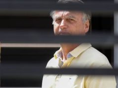 Jair Bolsonaro (PL) sério, de camisa amarela, atrás de grades