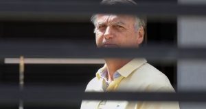 Jair Bolsonaro (PL) sério, de camisa amarela, atrás de grades