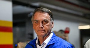 Bolsonaro de roupa de frio azul, sério, olhando para a câmera