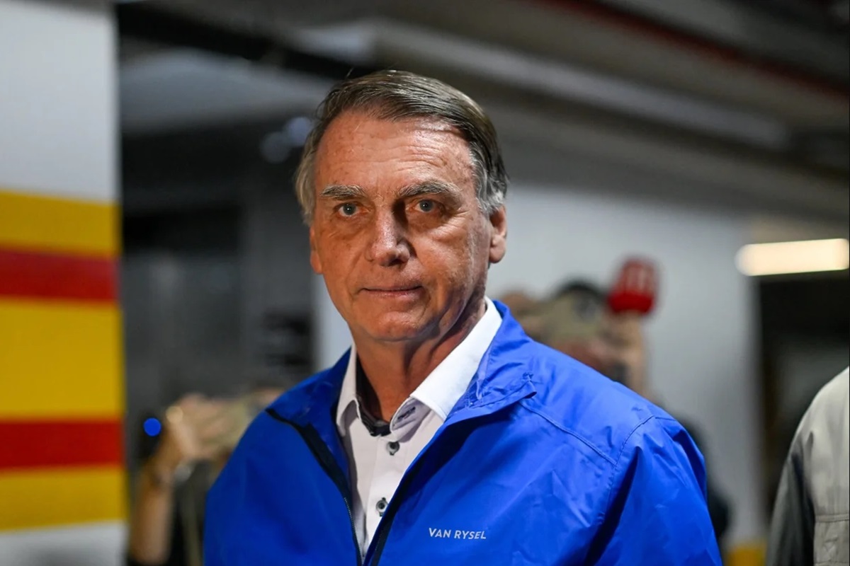 Bolsonaro de roupa de frio azul, sério, olhando para a câmera