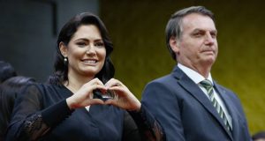 Michelle Bolsonaro ao lado de Jair Bolsonaro, ele sério e ela fazendo coração com as mãos