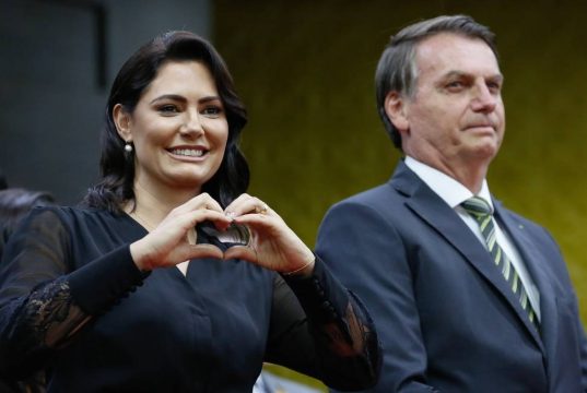 Michelle Bolsonaro ao lado de Jair Bolsonaro, ele sério e ela fazendo coração com as mãos