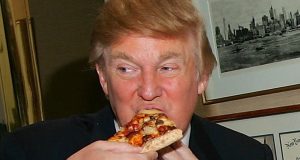 Donald Trump comendo fatia de pizza e olhando para o lado, em close