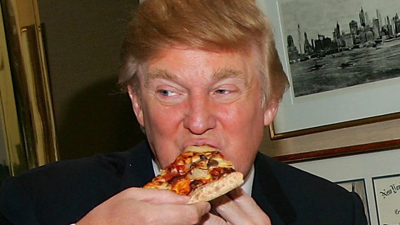 Donald Trump comendo fatia de pizza e olhando para o lado, em close