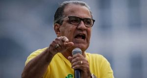 pastor Silas Malafaia de camisa verde e amarela e óculos de grau, falando em microfone e apontando, sério