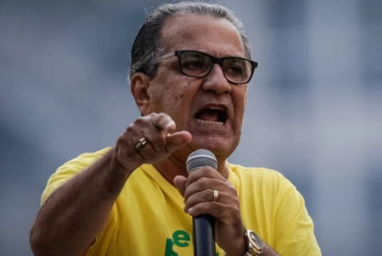 pastor Silas Malafaia de camisa verde e amarela e óculos de grau, falando em microfone e apontando, sério