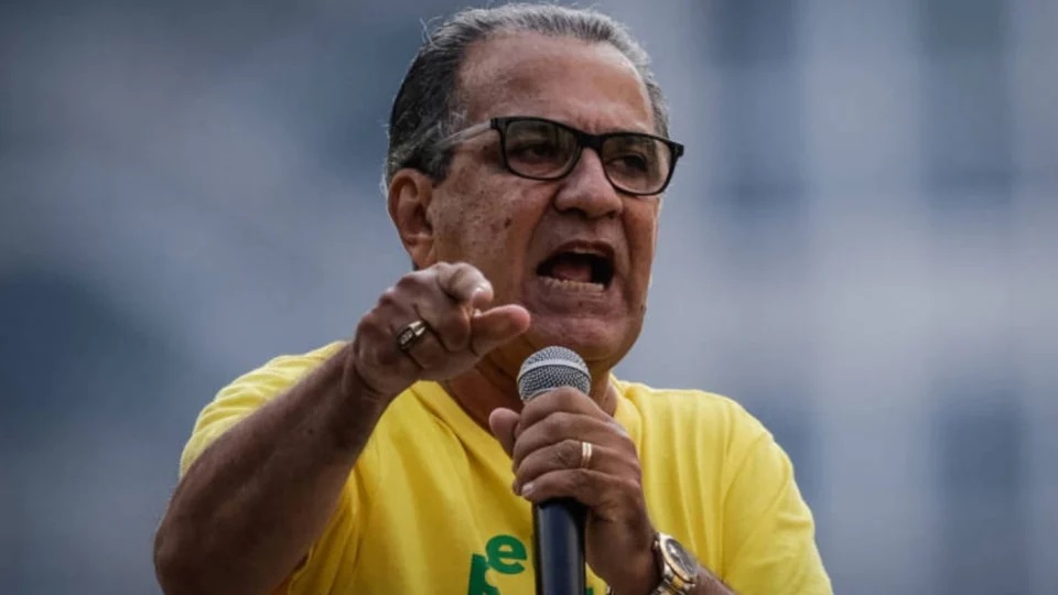 pastor Silas Malafaia de camisa verde e amarela e óculos de grau, falando em microfone e apontando, sério